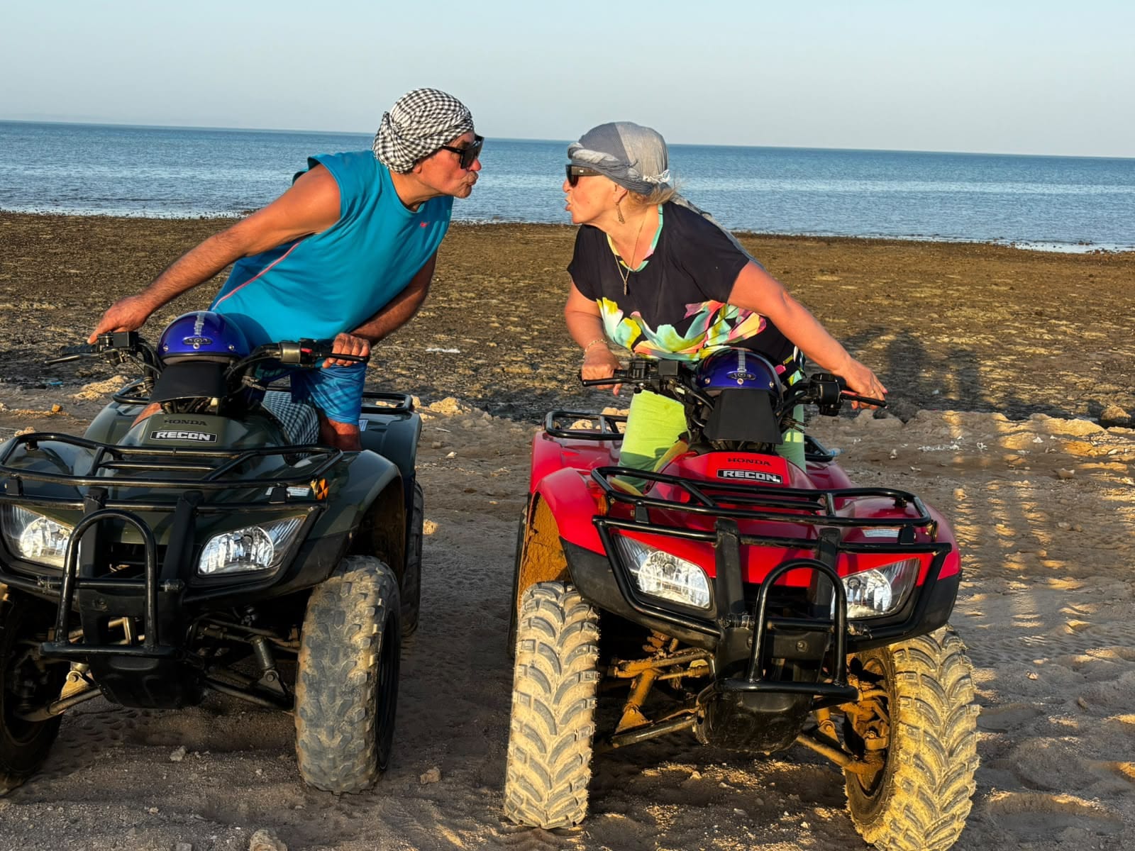 Two riders on quad bikes blowing kisses on the Red Sea shore in golden evening light